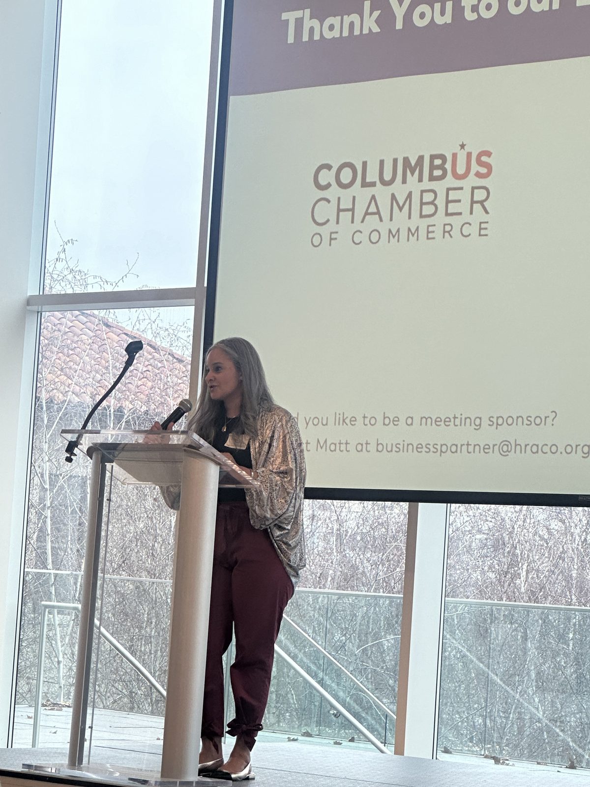 Dalia speaking at a podium with a Columbus Chamber of Commerce slide behind her